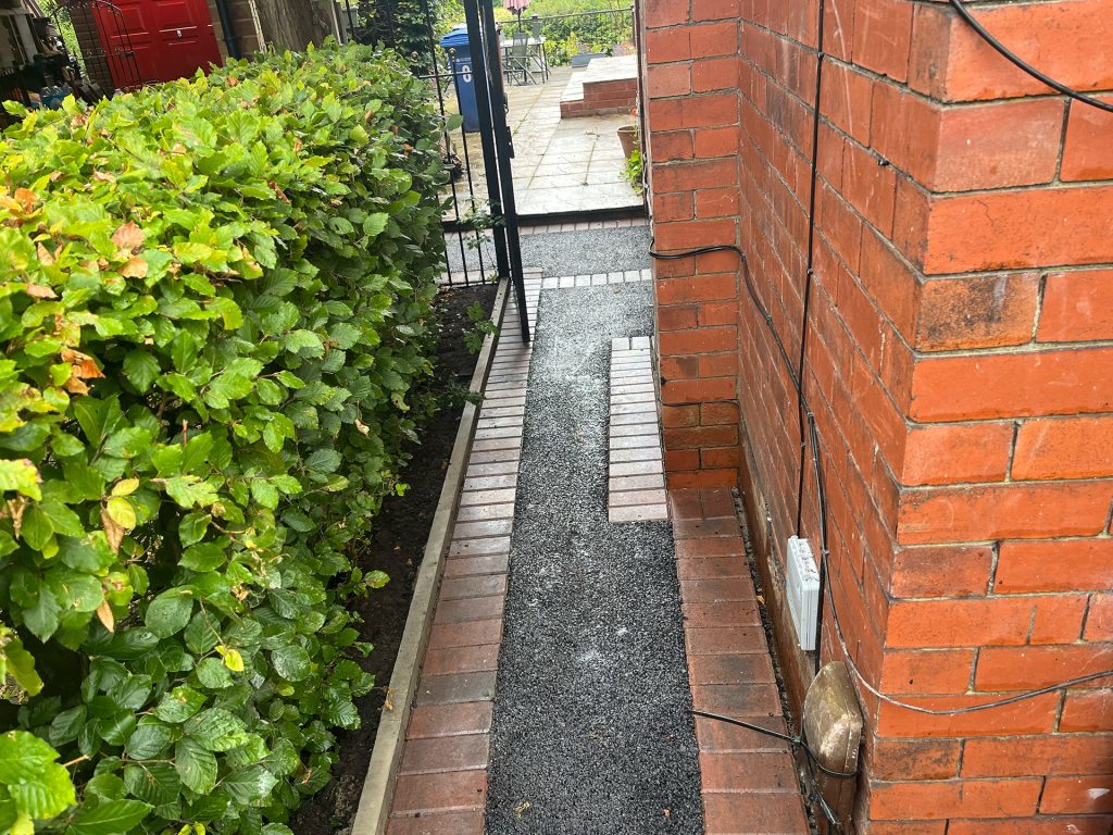 Tarmac pathway with red brick border going through a gate